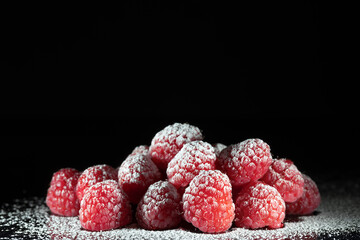 Ripe red raspberries with icing sugar being sprinkled on, shot against a dark background, low key image