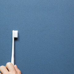 Hand holding a white toothbrush on navy blue background. top view, copy space
