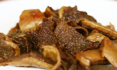 Braised beef tripe or bacem babat on white plate, wood background.