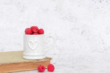 ripe raspberries shot against a light coloured background, wooden bowl, white china heart mug