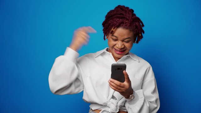 Successful afro woman recieved good news on smartphone and clenches fist, achieved her goal
