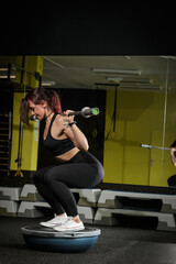 Concept of healthy lifestyle. Brunete training on bosu in the gym. Squats on bosu. Fitness girl....
