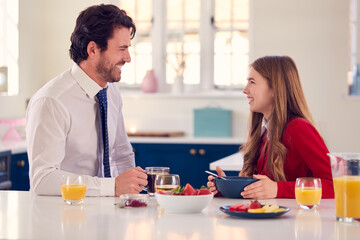 Father Wearing Suit Having Breakfast With Teenage Daughter In School Uniform At Home In Kitchen