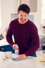 Man Cleaning Kitchen Counter With Spray And Cloth After Cake Baking