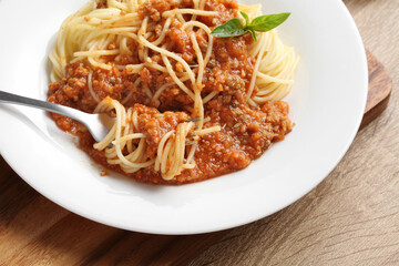 Close up a fork with spaghetti and red sauce in white dish on cutting board