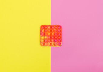 Pop it anti stress toy on a pink and yellow background, top view.