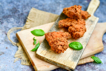 
 Crispy  deep fried   chicken strips and wedges potato. Breaded  with cornflakes chicken  breast fillets  with chilly peppers and fresh   basil on wooden rustic background