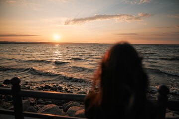 Blurred silhouette of a lonely woman looking at the sunset over the sea.