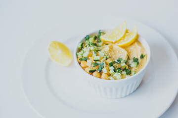 Hummus from chickpeas, with olive oil, lemon, sesame seeds and cucumbers, on white background.