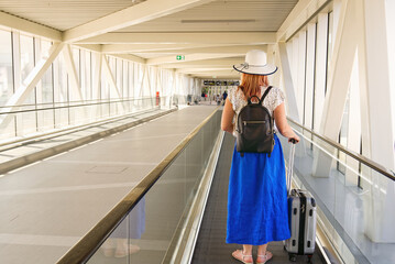 Young woman 40s no face with a carry-on baggage riding escalator in airport terminal. Safety...