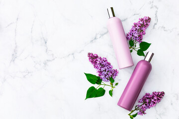 Two lilac bottles with shampoo and conditioner and lilac flowers on a marble background, top view,...