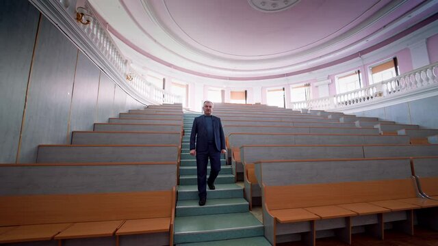 Professor in lecture hall. Male lecturer speaking on camera in empty auditorium in the university. Experienced teacher having a video lecture. Slow motion.