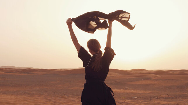 Portrait of a young Arab woman wearing traditional black clothing during beautiful sunset over the desert.