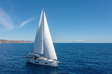 Sailing boat with open white sails, blue sky and rippled sea background