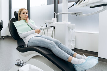 Cute, crooked woman touches sitting in a dental chair. The woman touches her cheek, she has a...