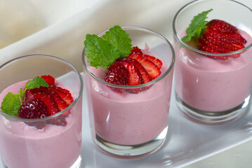 Strawberry dessert of milk and berries decomposed into cups on a wooden table decorated with fresh strawberries and mint leafs