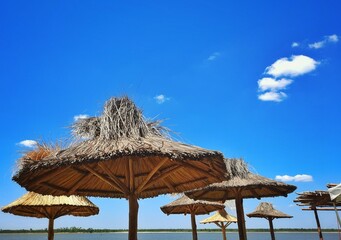 Straw beach umbrellas on blue sky background, horizontal