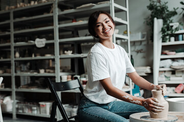 Beautiful happy asian girl making a clay vase in a workshop smiling and looking at the camera