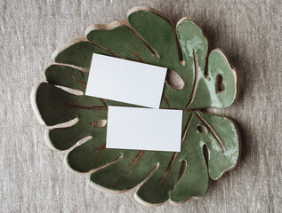Summer stationery still life. Blank business card mockup on ceramic plate of monstera sheet. Gray...