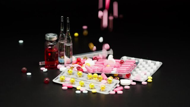 Close-up of falling coloured medicine tablets on black background, shooting of fallen red and yellow drugs and capsules on table. A lot of pills, the concept of the pharmaceutical industry.