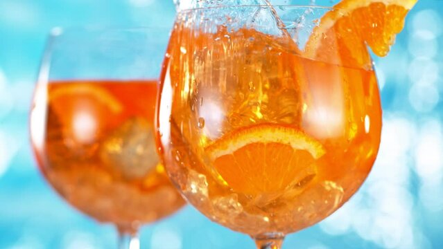 Super slow motion. Ice cube falling into glass of orange cocktail. Aperol spritz with sea surface background. Filmed on high speed cinematic camera at 1000 fps.