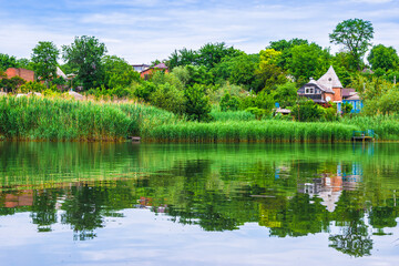 Fototapeta na wymiar Lake view. The lake reflects the house, reeds and trees. Reflection in the lake