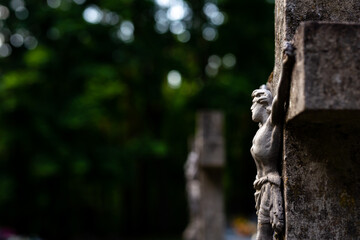 Jesus figurine on the cemetery cross. Picture taken in a soft light, shaded place.