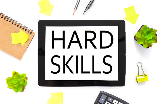 Hard Skills. the text is written on a white tablet screen. the tablet lies on a white workspace, near the notepad plant, arrows pointers to the tablet.