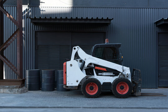 White Bobcat Forklift Truck On The Street Outside An Industrial Warehouse. Transportation Of Small Loads Using A Mini Loader. Warehouse Loader. Distribution. Delivery. Logistics. Transportation. 