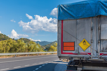 Rear view of truck with tipping semi-trailer for bulks with plate and label of dangerous goods for...
