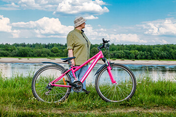 Obraz premium Elderly woman with a bicycle on the river bank. Grandma rides a bike.