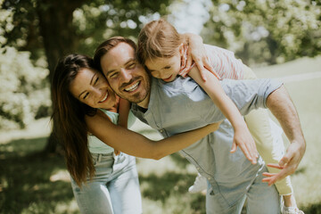 Fototapeta premium Happy young family with cute little daughter having fun in the park on a sunny day