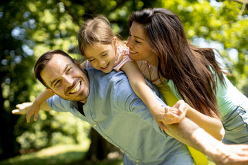 Fototapeta premium Happy young family with cute little daughter having fun in the park on a sunny day