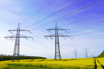 Above-ground power lines for energy supply. Yellow rape field and blue sky. Power pole for power...