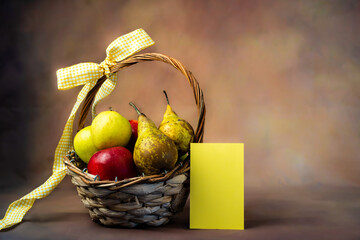 Scena con un cesto di frutta pieno di mele e pere rosse e gialle legato con un fiocco giallo con un...