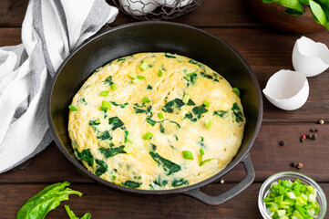 Omelette with spinach, green onions and feta cheese in a cast-iron frying pan on a dark wooden background. Healthy breakfast. Rustic style. Copy space.