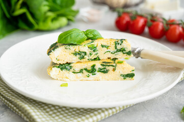 Omelette with spinach, green onions and feta cheese on a white plate on a gray concrete background. Healthy breakfast. Copy space.