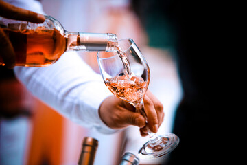 The waiter serves rose and white wine from the wine bottle in the wine glass at an event.