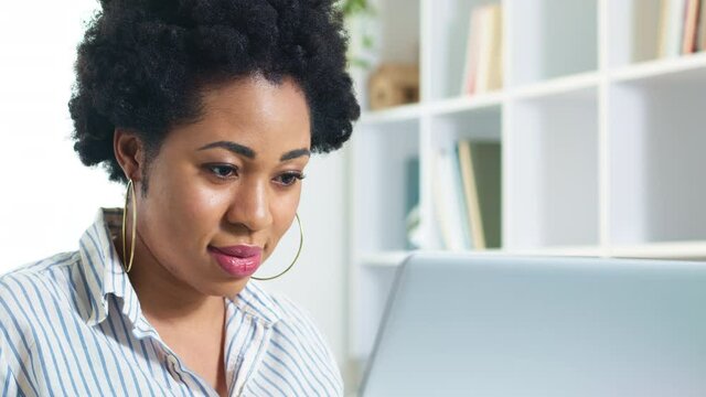 Close-up of the face of a black young woman working on a laptop. Portrait of an African female student education online. A female freelancer works remotely at home. 4K.