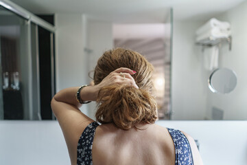 Fototapeta premium Woman from behind making a ponytail in her hair in front of the mirror.