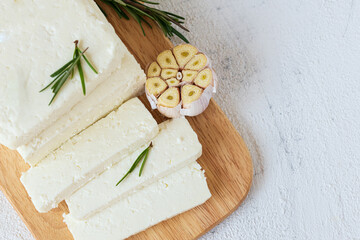 Fototapeta na wymiar Paneer, tofu, soy cheese, or brynza, feta with rosemary and garlic on a wooden cutting board on a light background
