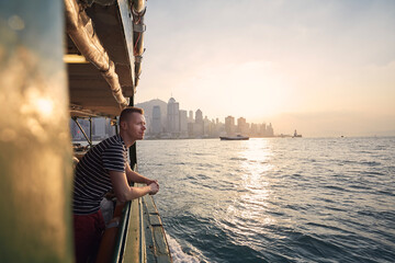 Pensive man looking from ferry boat against urban skyline st beautiful sunset. Tourist in Hong Kong.