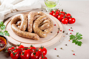 Raw meat sausages from beef and minced pork on wooden cutting board and products for cooking it close up