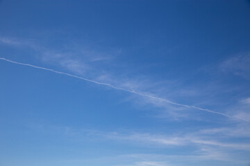 Fototapeta na wymiar Wide blue sky with few thin clouds and typical airplane trail cutting across the sky