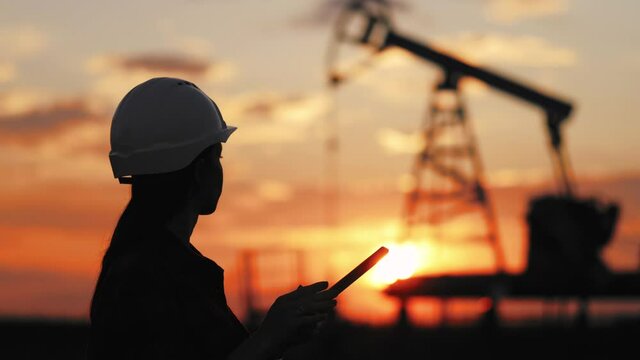 Industrial, oil and gas concept. Silhouette working engineer oil rig. Oil rigs at sunset. Silhouette of woman engineer with tablet overseeing the site of crude oil production at sunset.