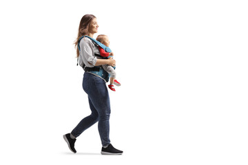 Full length profile shot of a mother walking and carrying a baby in a carrier