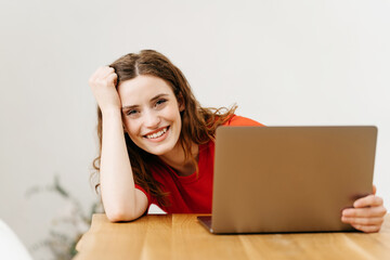 Happy friendly young woman peering around her laptop
