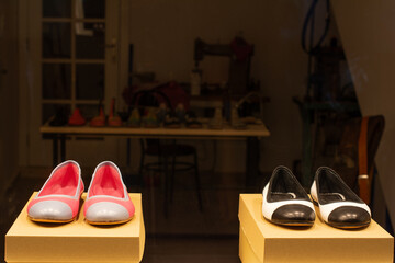 Novi Sad, Serbia – June 15, 2021: Danila Kisa street. Two pairs of shoes are lying on display pedestals in a window display of a shoemaker workshop at night.  - Powered by Adobe