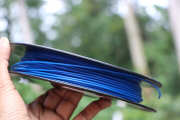 Spool of blue color wire called as 3D Printer filament held in hand on nature background