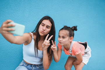 Teenage girl using smartphone for taking a selfie with her little cute sister - Generation z and technology concept
